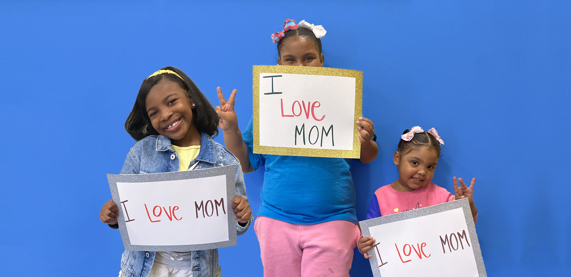 Three grateful children holding signs that read 'I love mom'