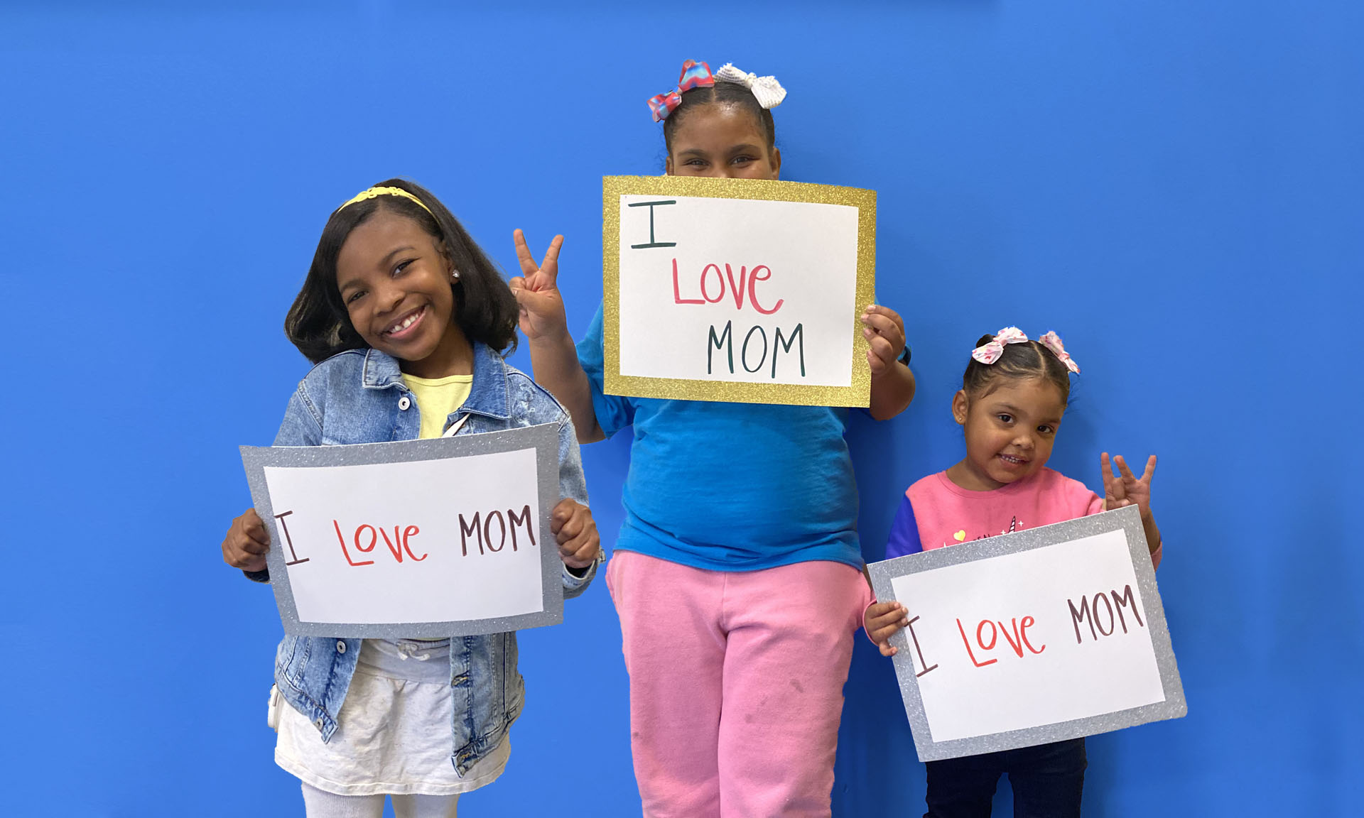 Three grateful children holding signs that read 'I love mom'